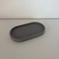 A dark gray, oval-shaped jesmonite tray with a raised rim, photographed on a light gray surface against a white background.