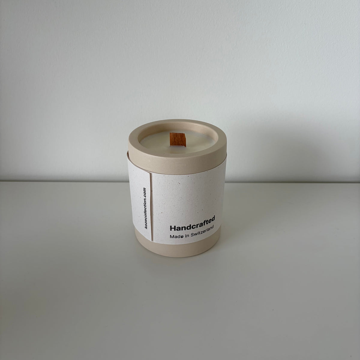 A minimalist soy wax candle in a cylindrical kraft paper container with a white paper label, set against a clean, light gray background.